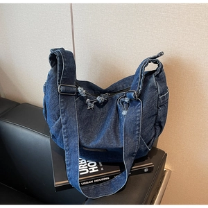 Detailed close-up of dark blue denim shoulder bag with metal buckle and zipper fringe