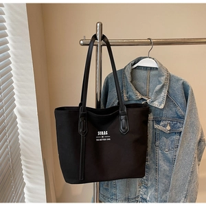 Detail of black canvas tote bag hanging next to denim jacket with brand logo SOBAG