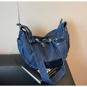 Detailed view of dark blue denim bag showing frayed edges and branded leather logo