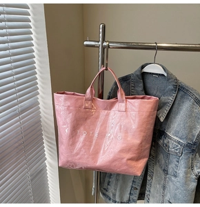 Detail einer glänzenden rosa Tragetasche mit weißem TOTE BAG Aufdruck am Bügel