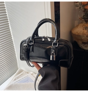 Detail of black patent leather handbag with silver lock and circular handles on white fabric