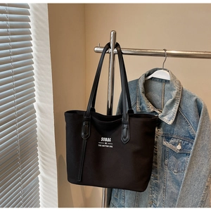 Close-up of black canvas tote bag with white SOBAG logo hanging against a soft background