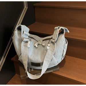 Detail of light blue denim hobo bag featuring frayed edges and vintage brown leather patch