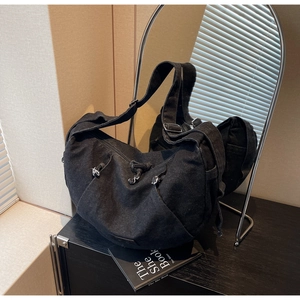 Detail of black denim crossbody bag featuring drawstring pleats and side pockets