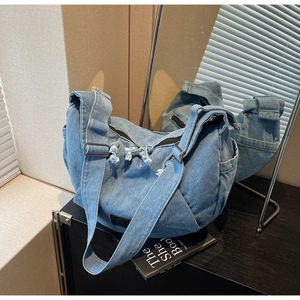 Detail of light blue washed denim crossbody bag with fringe pleats on a black cabinet