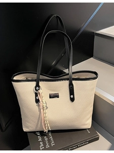 Cream canvas tote bag with black trim and tassel detail on a minimalist stair background