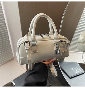 Detail view of white Boston handbag featuring silver buckles and smooth matte texture