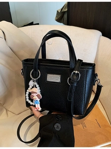 Chic black lychee leather bucket bag with pearl doll charm and adjustable strap