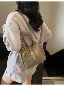 Taupe minimalist bucket bag with gold lock and dog charm shown in indoor setting