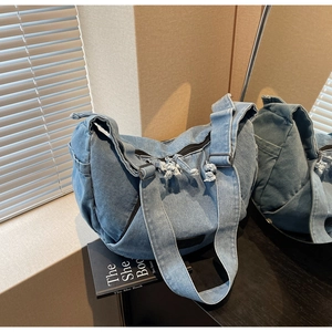 Detail of light blue denim half-moon bag with wide strap and zipper knot on a black table