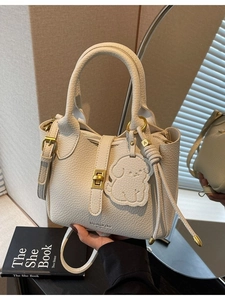 Minimalist beige pebble leather bucket bag with dog charm and gold twist lock detail