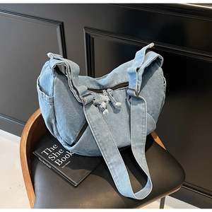 Detail of light blue denim hobo bag showing texture, frayed tassels and metallic buckle