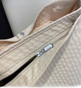 Detail of smooth silver metal zipper on striped beige fabric shoulder bag with neat stitching