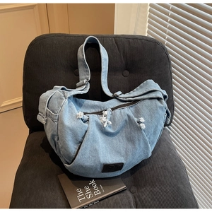 Detail of light blue denim crossbody bag featuring frayed edges and black logo patch