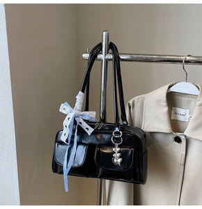 Detail of a black shoulder bag with dual front pockets and heart charm on a trench coat