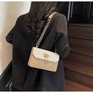 Détail du sac à chaîne pailleté avec fermoir oreilles de chat sur fond de blazer noir