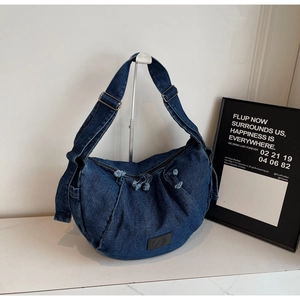 Detail of dark blue denim crescent bag showing knotted zipper and textured fabric