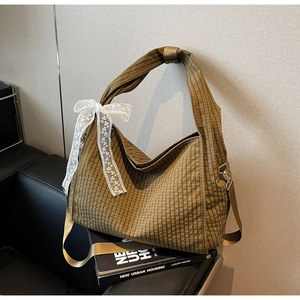 Detail of a brown plaid hobo bag with a white lace bow and adjustable shoulder strap