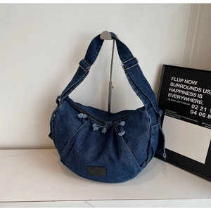 Detail of blue denim hobo bag featuring drawstring pleats and adjustable metal buckles