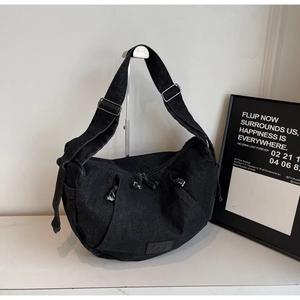 Detail of black washed denim crossbody bag featuring adjustable drawstring and logo patch