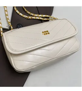 Macro detail of white chevron-quilted leather bag with gold chain strap and metal logo