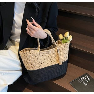 Detail of two-tone woven straw tote bag with black base and beige top featuring a tassel