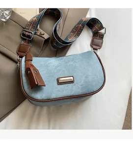 Detail of blue denim crossbody bag with brown trim and colorful bohemian strap