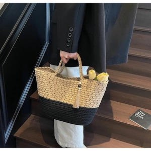 Close-up of contrast color woven tote bag with fringe charm on a wooden staircase
