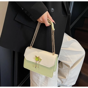 Détail d'un sac bandoulière en cuir crème et vert avec boucle chat et gland