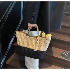Detail of handwoven two-tone straw tote bag with decorative tassel and wooden beads