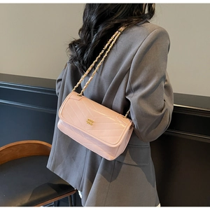Detail of light pink quilted crossbody bag with gold chain strap on a grey blazer