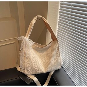 Detail of off-white hobo bag with textured fabric and large white lace bow accent