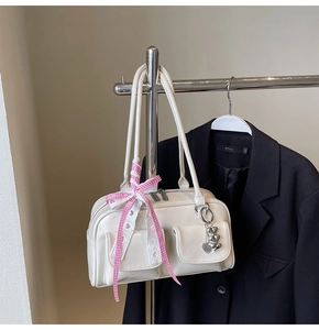 Detail of cream bowling bag with front pockets and pink plaid ribbon with heart charm