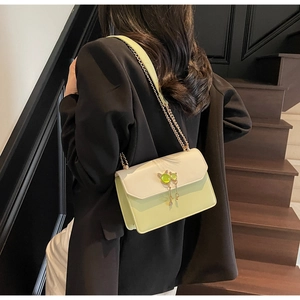 Détail du sac à bandoulière bicolore élégant avec boucle chat dorée sur l'escalier