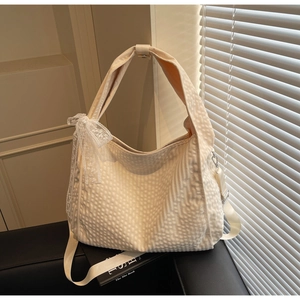 Detail view of cream tote bag with textured grid pattern and white lace bow decoration