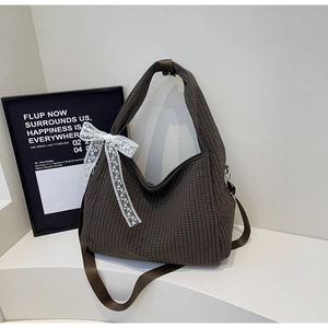 Detail of dark brown checkered canvas tote bag with a white lace bow charm and soft structure