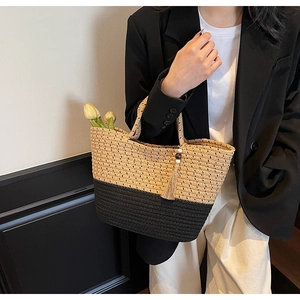 Detail of hand-woven straw tote bag with black and beige contrast and tassel wooden bead charm