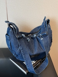 Distressed dark blue denim crossbody bag with frayed edges and wide shoulder strap