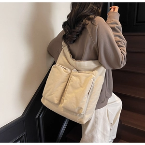 Lifestyle view of a beige canvas tote bag with front pockets on a model on wooden stairs
