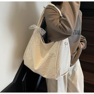 Detail of cream-white quilted tote bag featuring a delicate lace bow charm and D-ring buckle