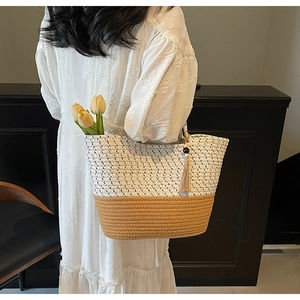 Detail of two-tone woven straw tote bag featuring tassel charm and contrast texture