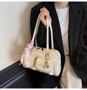 Detail of cream shoulder bag featuring dual front buckle pockets and heart charm