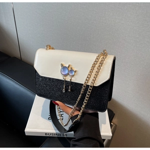 Détail d'un sac à chaîne bicolore élégant avec une boucle en pierre précieuse chat