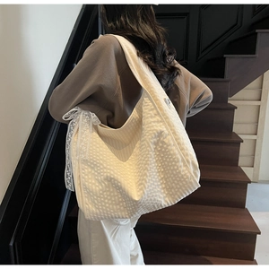 Close-up of a cream-white tote bag with waffle texture and delicate lace bow detail