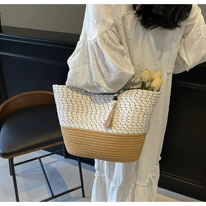 Detail of two-tone woven straw tote bag with tassel charm and wooden beads on a white dress