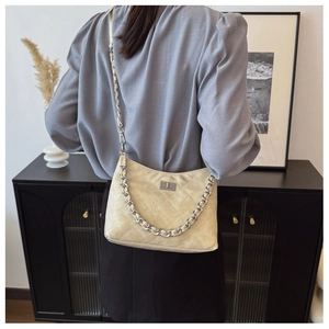 Beige Stepp-Schultertasche mit Metallkette, getragen von einem Modell in modernem Raum