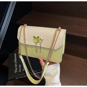 Détail du sac bandoulière vert et beige avec fermoir chat doré sur l'escalier