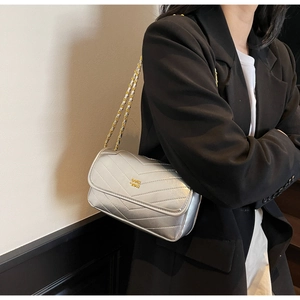 Detail of silver V-quilted shoulder bag with gold chain strap worn by a model