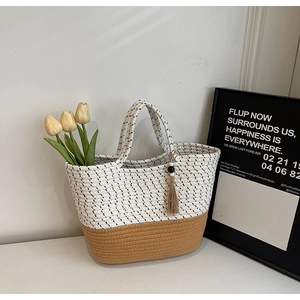 Detail of woven tote bag featuring two-tone contrast design and bohemian tassel ornament