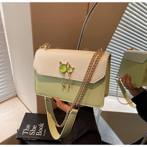 Détail du sac en cuir vert et beige avec un bijou chat et une bandoulière en chaîne